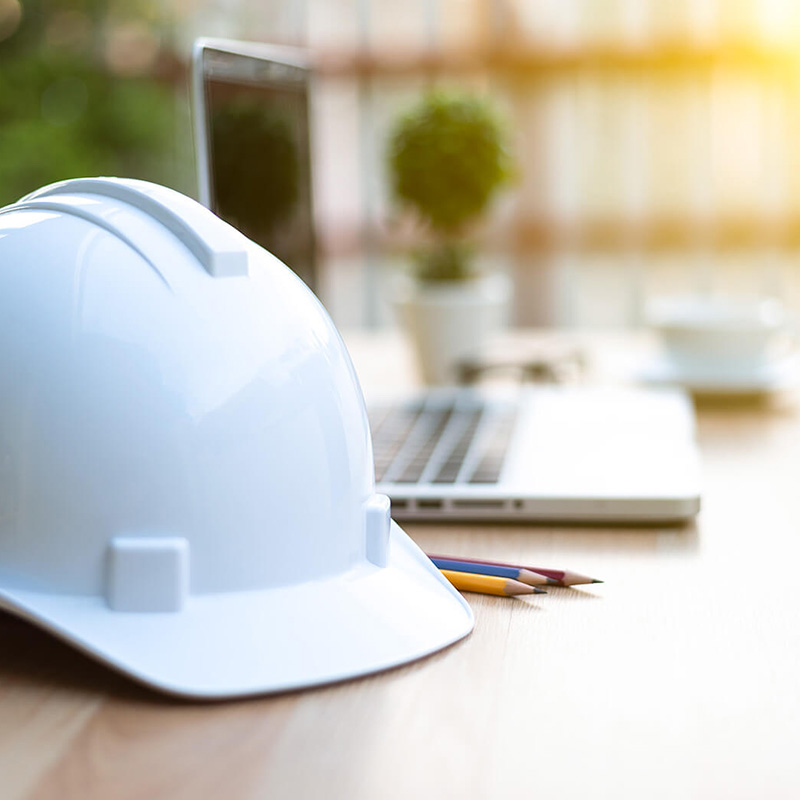 a white hard hat sits on a table next to a laptop and pencils.