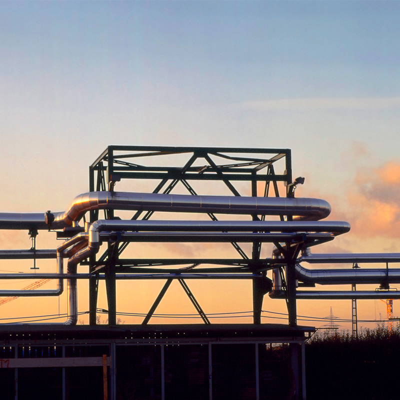 a large metal structure with pipes and a sunset in the background.